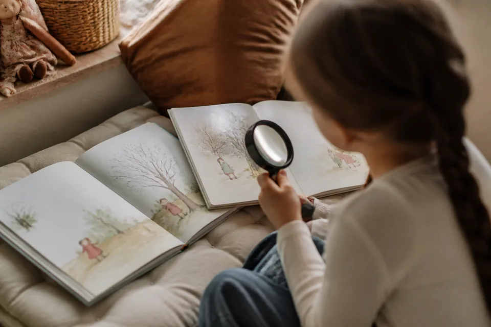 Un enfant compare deux livres illustrés ouverts avec une loupe