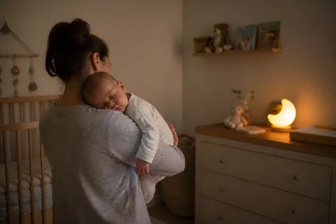 Uma mãe segura o bebê dormindo no ombro ao lado do berço